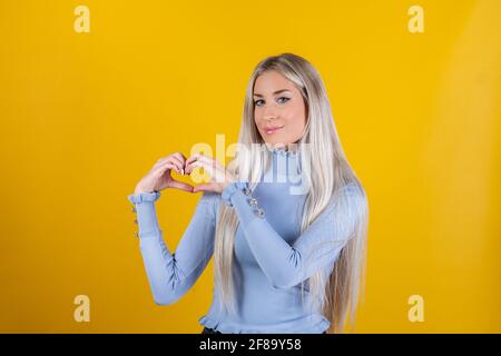 Femme montre le geste de coeur, exprime l'amour sur fond jaune - fille fait le geste de coeur, a l'expression heureuse. Concept de relation et langage corporel Banque D'Images