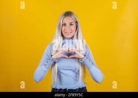 Femme montre le geste de coeur, exprime l'amour sur fond jaune - fille fait le geste de coeur, a l'expression heureuse. Concept de relation et langage corporel Banque D'Images