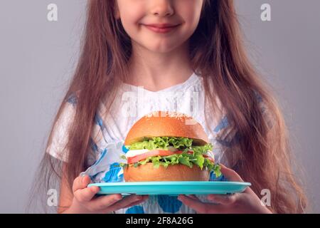 Petite fille mangeant un gros hamburger. Enfant regardant un gros sandwich sain, studio isolé sur fond blanc. Banque D'Images