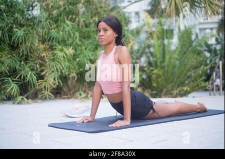 Portrait d'une jeune femme afro-américaine s'étirant en yoga Posez à l'extérieur pendant la journée avec un fond vert tropical Banque D'Images