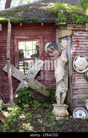 Une statue usée s'étend depuis le coin d'une grange rustique, une vie encore humoristique dans ce magasin d'antiquités en plein air original Banque D'Images