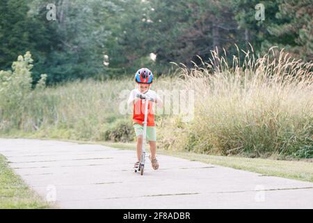 Petit garçon dans un casque de sport à cheval sur route rue dans le parc le jour d'été. Activités saisonnières en plein air pour les enfants. Vie saine de l'enfance Banque D'Images