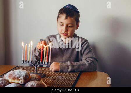 Garçon en kippah éclairant des bougies sur une menorah pour les vacances traditionnelles juives d'hiver Hanukkah. Enfant célébrant le festival des lumières de Chanukah à la maison. Banque D'Images