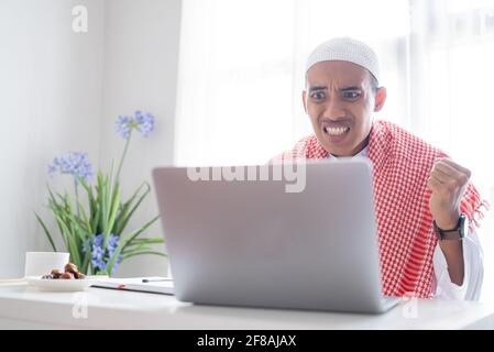 homme musulman en colère en regardant l'écran de son ordinateur portable Banque D'Images