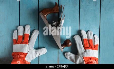 Un menuisier en gants regarde la jointer, qui se trouve sur une table bleue. Il fabrique des produits en bois Banque D'Images