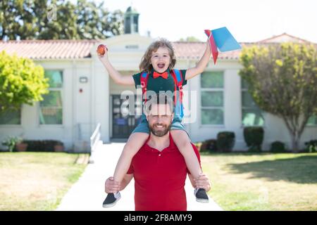 L'homme et l'enfant excités surpris de son porcgyback près de l'école. Le père et le fils courent avec le père après être revenus de l'école. École, famille, éducation et Banque D'Images