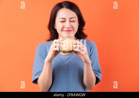 Jeune femme asiatique mangeant un hamburger sur fond orange Banque D'Images