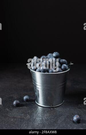 Myrtille fraîche et mûre dans un petit seau en métal sur fond noir. Baies de bleuets juteuses pleines de vitamines. Banque D'Images