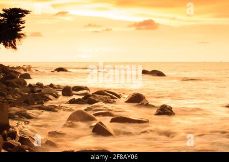 Un paysage marin tranquille au crépuscule de l'été. Des nuages spectaculaires et un ciel de coucher de soleil, des vagues douces de l'océan s'écrasant sur la plage des rochers. Khao Lak Beach, Thaïlande. Banque D'Images