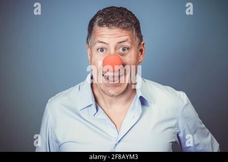 Homme d'âge moyen avec chemise bleue et nez clown rouge posé sur fond bleu dans le studio Banque D'Images