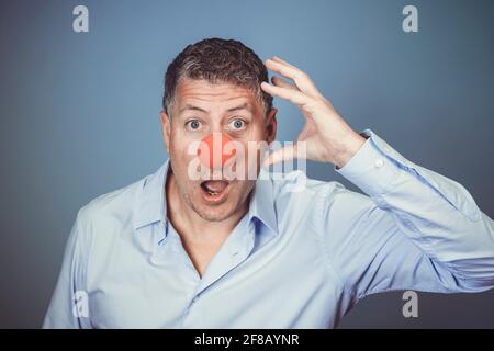 Homme d'âge moyen avec chemise bleue et nez clown rouge posé sur fond bleu dans le studio Banque D'Images