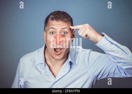 Homme d'âge moyen avec chemise bleue et nez clown rouge posé sur fond bleu dans le studio Banque D'Images