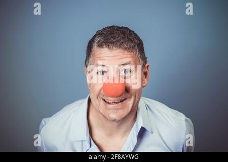 Homme d'âge moyen avec chemise bleue et nez clown rouge posé sur fond bleu dans le studio Banque D'Images