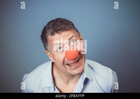 Homme d'âge moyen avec chemise bleue et nez clown rouge posé sur fond bleu dans le studio Banque D'Images