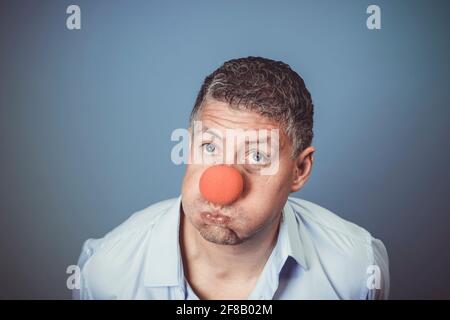 Homme d'âge moyen avec chemise bleue et nez clown rouge posé sur fond bleu dans le studio Banque D'Images