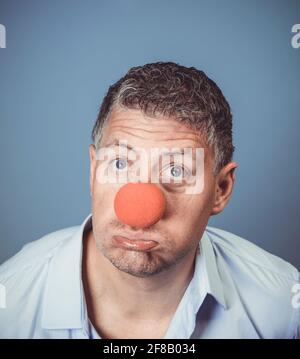 Homme d'âge moyen avec chemise bleue et nez clown rouge posé sur fond bleu dans le studio Banque D'Images