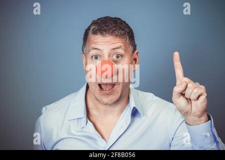 Homme d'âge moyen avec chemise bleue et nez clown rouge posé sur fond bleu dans le studio Banque D'Images