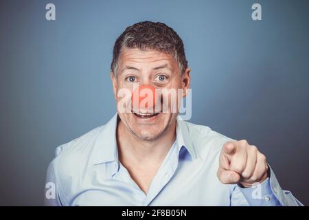 Homme d'âge moyen avec chemise bleue et nez clown rouge posé sur fond bleu dans le studio Banque D'Images