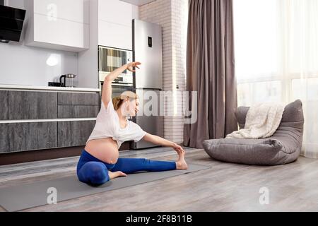 sportive maman-to-be stretching jambes pendant l'entraînement à la maison, femme forte flexible dans les jambes et t-shirt se préparant pour l'entraînement de yoga, chaud muscl de corps Banque D'Images