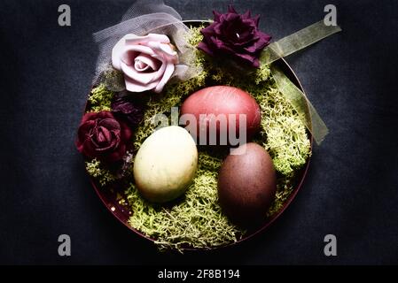 œufs de pâques teints dans un bol décoratif avec mousse et roses Banque D'Images