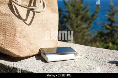 Power Bank charge un smartphone sur le front de mer près de la maquette du sac de plage. Un chargeur de voyage portable. Banque D'Images