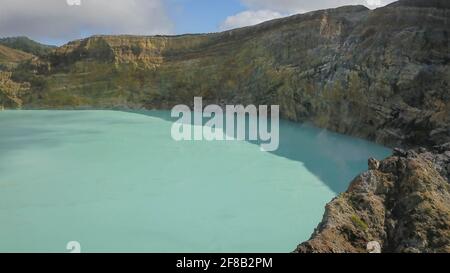 Vol au-dessus des lacs de Vulanice à basse altitude. Vue rapprochée d'un mur de roche séparant les lacs colorés. Cratère volcanique de trois couleurs Kelimutu couvert Banque D'Images