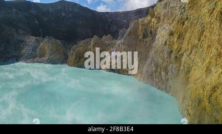 Vol au-dessus des lacs de Vulanice à basse altitude. Vue rapprochée d'un mur de roche séparant les lacs colorés. Cratère volcanique de trois couleurs Kelimutu couvert Banque D'Images