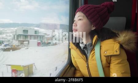 Portrait de style de vie d'une jeune femme japonaise asiatique heureuse et belle dans une veste et un chapeau jaunes regardant à travers la fenêtre du train en voyage pendant les vacances d'hiver Banque D'Images