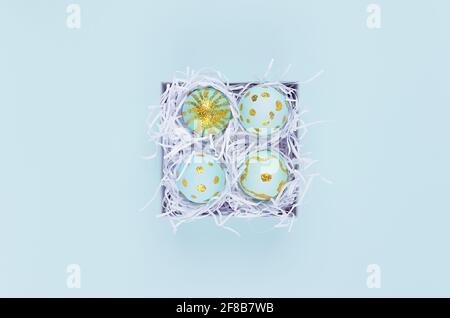 Œufs de pâques faits main bleus avec motif doré pailleté dans une boîte cadeau sur fond bleu, vue du dessus. Banque D'Images