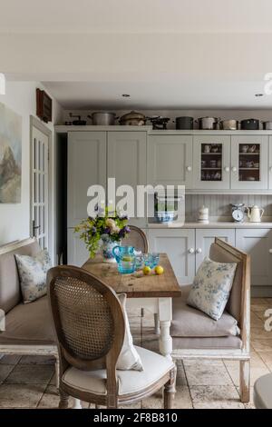 Cuisine de style Shaker avec bancs Gustavian et sol travertin dans les années 1930 West Sussex rénovation côtière.