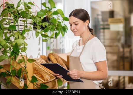 Femme en tablier regardant la chemise dans la boutique de boulangerie Banque D'Images