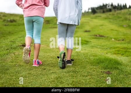 Les enfants qui font de la randonnée dans les montagnes ou les prairies avec des chaussures de randonnée sport. Les filles marchent sur le sentier de montagne en portant des bottes de montagne et des bâtons de marche. FR Banque D'Images