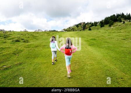 Les enfants qui font de la randonnée dans les montagnes ou les prairies avec des chaussures de randonnée sport. Les filles marchent sur le sentier de montagne en portant des bottes de montagne et des bâtons de marche. FR Banque D'Images