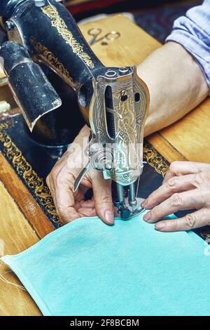 Femme mûre couturière feuille de couture de tissu vert clair avec machine-outil vintage noire à la table en bois dans la chambre de près Banque D'Images