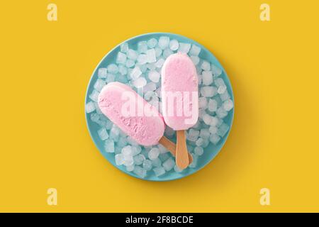 Des pop-glaces aux fraises et de la glace pilée sur une assiette bleue sur du jaune arrière-plan Banque D'Images