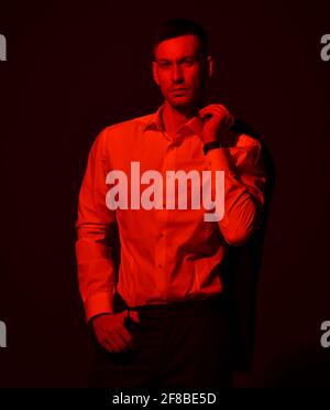 Un jeune homme d'affaires plein de confiance, yuppie, en costume officiel, tient la veste sur son épaule. Filtre de lumière rouge, gel Banque D'Images