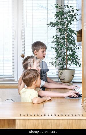 Les écoliers blonds intéressés regardent l'affichage d'ordinateur et les garde d'enfants mains sur la souris et le clavier assis au bureau avec pot usine Banque D'Images