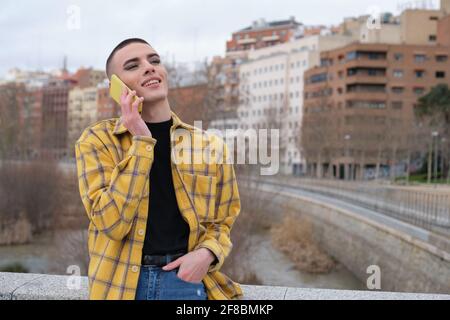 Jeune personne non binaire parlant sur un smartphone riant. Faites le maquillage de la personne androgyne. Banque D'Images