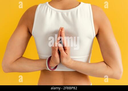 Jeune femme faisant l'exercice de yoga sur le tapis dans Virasana ou Hero pose avec la prière inversée ou namaste dans fond jaune. Banque D'Images