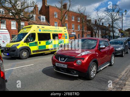 Beaconsifield, Buckinghamshire, Royaume-Uni. 13 avril 2021. Nous vous rappelons que Covid-19 n'est toujours pas parti car une ambulance d'urgence passe la file d'attente. Beaconsfield était aujourd'hui plus occupé alors que les gens étaient à l'extérieur et au sujet de profiter du soleil de printemps et de la prochaine étape dans la feuille de route Covid-19 d'assouplissement du verrouillage. Bienvenue Retour des panneaux ont été placés autour de la ville par Buckinghamshire Council. Crédit : Maureen McLean/Alay Live News Banque D'Images