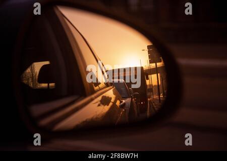 Vue à travers les miroirs de voiture sur les voitures, bus et coucher de soleil dans la grande ville Banque D'Images