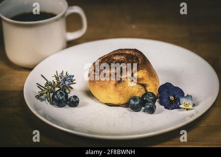 Roulé à la cannelle sur une assiette de bleuets et de fleurs Banque D'Images