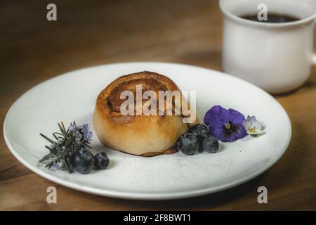 Roulé à la cannelle sur une assiette de bleuets et de fleurs Banque D'Images