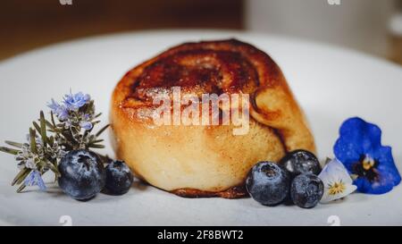 Roulé à la cannelle sur une assiette de bleuets et de fleurs Banque D'Images