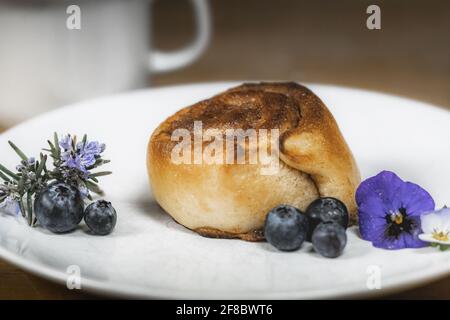 Roulé à la cannelle sur une assiette de bleuets et de fleurs Banque D'Images