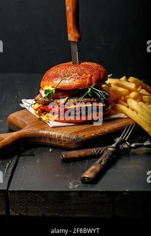Un hamburger de bœuf double appétissant et une portion de frites sur une planche à découper en bois. Arrière-plan rustique sombre. Photographie de la restauration rapide STILL Life. Sho vertical Banque D'Images