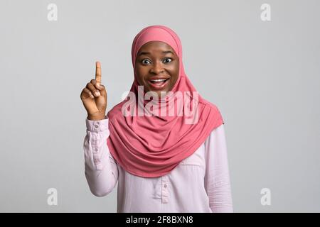 Femme noire inspirée pointant du doigt vers le haut, fond gris Banque D'Images