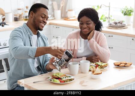 Couple de Noirs affectueux manger un délicieux petit déjeuner et boire un café à l'intérieur Cuisine Banque D'Images