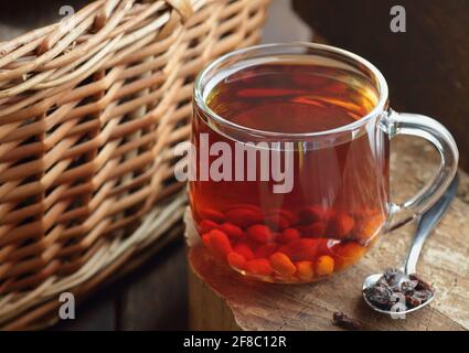 Thé de baie de Goji dans une tasse de verre sur bois rustique avec osier à proximité, gros plan, naturopathie, médecine naturelle, ayurveda concept, rustique, pays, lent l Banque D'Images