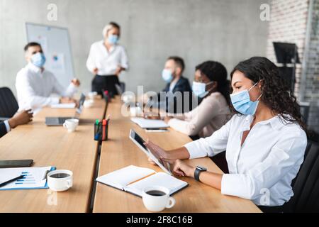 Femme d'affaires en masque de visage utilisant une tablette pendant une réunion d'entreprise en intérieur Banque D'Images